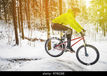 Silhouette eines Radfahrers in einem Sprung. Mountainbiken auf Wanderwegen in einem verschneiten Wald. Extreme Winter Sport. Bike Reiter fliegt durch die Luft, Stockfoto