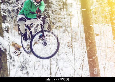 Silhouette eines Radfahrers in einem Sprung. Mountainbiken auf Wanderwegen in einem verschneiten Wald. Extreme Winter Sport. Bike Reiter fliegt durch die Luft, Stockfoto