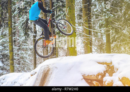 Silhouette eines Radfahrers in einem Sprung. Mountainbiken auf Wanderwegen in einem verschneiten Wald. Extreme Winter Sport. Bike Reiter fliegt durch die Luft, Stockfoto