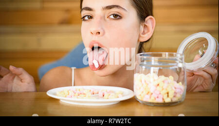 Süßen Zahn. Candy Girl mit süßem Gebäck. Pretty Woman halten Marshmallows auf der Zunge. Lustige Frau genießen essen Marshmallows. Junk Food. Ungesunde und schädliche Lebensmittel. Süße Snack Stockfoto