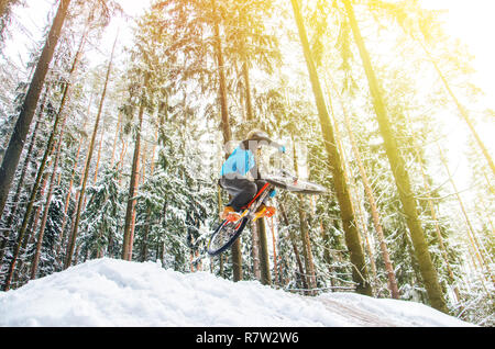 Silhouette eines Radfahrers in einem Sprung. Mountainbiken auf Wanderwegen in einem verschneiten Wald. Extreme Winter Sport. Bike Reiter fliegt durch die Luft, Stockfoto