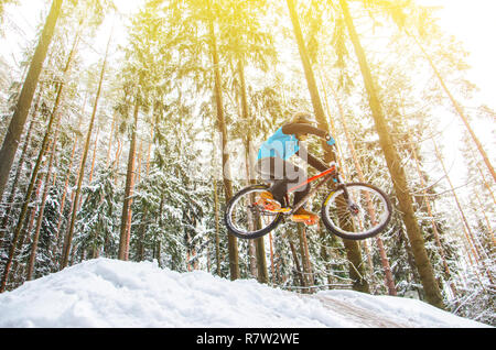 Silhouette eines Radfahrers in einem Sprung. Mountainbiken auf Wanderwegen in einem verschneiten Wald. Extreme Winter Sport. Bike Reiter fliegt durch die Luft, Stockfoto