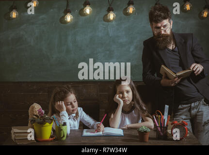 Langweilig Lektion Konzept. Lehrer und Schüler Mädchen im Klassenzimmer, schwarzes Brett für den Hintergrund. Mann mit Bart unterrichtet Schülerinnen, Buch zu lesen. Gelangweilt und müde Kinder hören Lehrer. Stockfoto