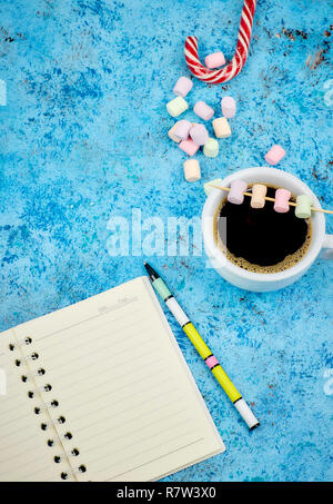 Tasse mit Kaffee und Marshmallows, leer, öffnen Sie Notizbuch mit Kugelschreiber auf abstrakten blauen Hintergrund. Ansicht von oben. Flache mockup. Platz für Text. Stockfoto