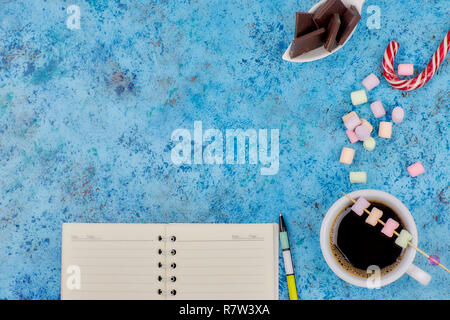 Tasse mit Kaffee und Marshmallows, leer, öffnen Sie Notizbuch mit Kugelschreiber auf abstrakten blauen Hintergrund. Ansicht von oben. Flache mockup. Platz für Text. Stockfoto