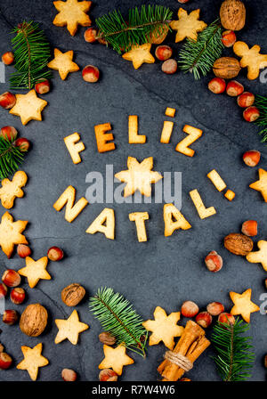 FELIZ NATAL COOKIES. Wörter Frohe Weihnachten en Portugiesisch mit gebackenen Plätzchen, Weihnachtsschmuck und Muttern auf schwarzem Schiefer Hintergrund. Weihnachtskarte für Portugiesisch sprechenden Länder der Ansicht von oben. Stockfoto