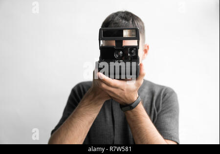 Hübscher junger bärtiger Mann in einem schwarzen T-Shirt, Vintage altmodischen Film Kamera auf einem weißen Hintergrund und Suchen in den Suchermodus der Kamera Stockfoto