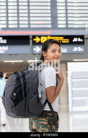 Reisen Frau mit einem Rucksack auf dem Rücken unter einem Schild mit den Flugverbindungen. Die asiatische Mädchen mit dem Gepäck ist unter Vorstand am Flughafen. Stockfoto