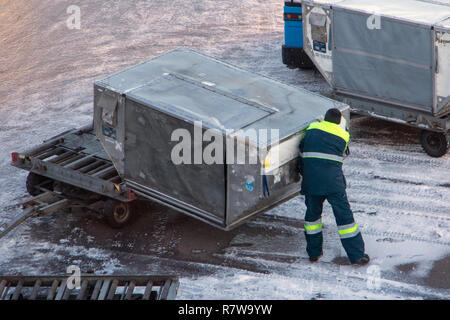 Ein Bodenpersonal des Flughafens die Frachtcontainer manipulieren. Der Mann ist das Laden einer großen schweren Container auf einer Karre auf Winter Flughafen. Stockfoto