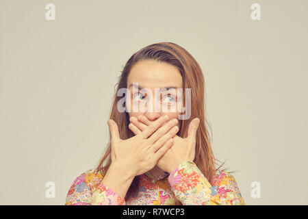 Überrascht junge Frau deckt ihren Mund mit den Händen, steht auf einem weißen Hintergrund. Augen zur Seite. Stockfoto