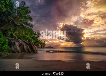 Sonnenstrahlen bei Sonnenuntergang hinter einer großen Wolke im Anse Georgette auf Praslin auf den Seychellen Stockfoto