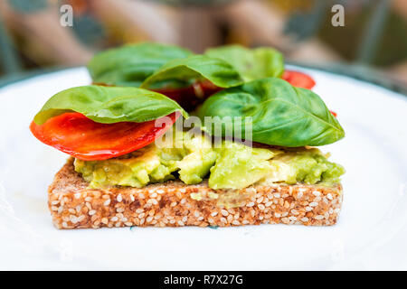 Nahaufnahme von slice Stück ganze Saat aufsproßte geröstetes Brot auf dem Teller mit roten Tomatenscheiben, grüne Blätter Basilikum, und Avocado bruschetta auf Plat Stockfoto