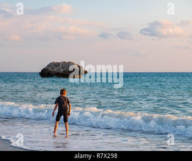 Eine barfüßige Junge spielt an der Strand von Petra tou Romiou Felsen, in Paphos, Zypern. Der Strand ist der Geburtsort der Aphrodite in der Griechischen my angesehen Stockfoto