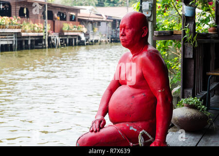 Eine Statue von einem thailändischen Mann in Rot lackiert, durch den Fluss Chao Phraya im Baan Silapin Artist's House, Bangkok, Thailand Stockfoto
