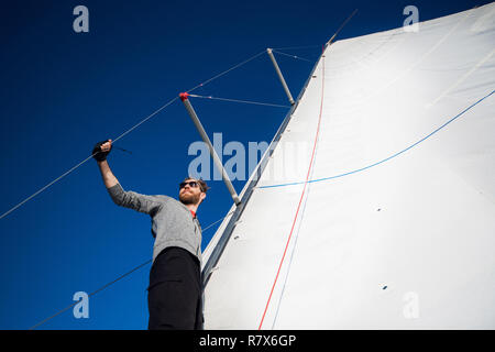 Schöne und selbstbewusste junge Mann steht auf Yachtcharter board und im Meer durch die Brille schauen. Er liegt am Rande der Yacht. Guy Holding segeln Seil in der Hand. Junge Mann ist glücklich und friedlich. Stockfoto