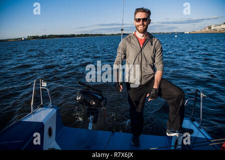 Junger Mann mit Sonnenbrille auf Yachtcharter stern und genießen Sie perfekte Herbst Tag unter Segeln - segelurlaub Konzept Stockfoto