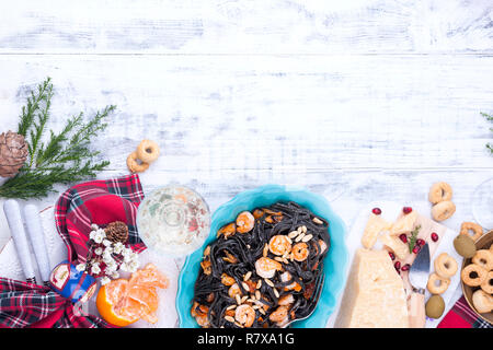 Weihnachtsessen in Italien für den Urlaub. Pasta ist schwarz mit Meeresfrüchten und verschiedenen Snacks, Wein und Parmesan Käse. Draufsicht und heller Holzhintergrund Stockfoto