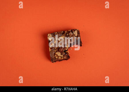 Gebissen brownie Kuchen Stück auf eine orange farbigen Hintergrund über Anzeigen in minimalistischem Stil. Schokolade Dessert mit reichlich Walnüssen dekoriert Stockfoto