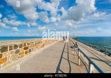 Touristen zu Fuß der Küste Promenade in der Nähe der Kleinen grün weiß Leuchtturm in Warnemünde Rostock Deutschland Hafen ein Schiff in der Ferne Kreuzfahrten Stockfoto