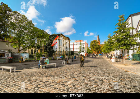 Touristen und Einheimische Deutsche Spaziergang durch den Hauptplatz Schnittpunkt der Coastal Resort City von Warnemünde, mit der Turm der Kirche im Blick. Stockfoto