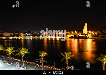 Vollmond über der Küste Hafen von Brindisi, Italien, wie der italienische Seefahrer Denkmal, die Bucht und die Promenade sind an einem sommerlichen Abend beleuchtet. Stockfoto