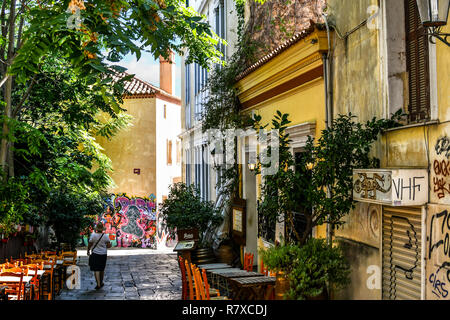 Ein solo Frau touristische Wanderungen vorbei an einem kleinen Café mit Tischen im Freien auf einem schmalen schattigen Gasse im Plaka Viertel von Athen, Griechenland Stockfoto