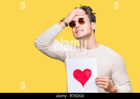 Jungen gutaussehenden Mann holding Karte mit roten Herzen über isolierte Hintergrund mit Hand betonte am Kopf, mit Scham und Überraschung Gesicht schockiert, wütend und fr Stockfoto