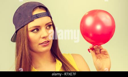 Junges Mädchen, lustig dumme Gesichter. Junge trendige Frau in Jeans cap halten roten Ballon. Stockfoto