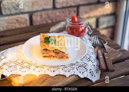Klassische hommade Lasagne mit Bolognese Sauce auf Holztisch mit Spitze Tischdecke Stockfoto