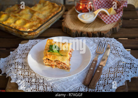 Klassische hommade Lasagne mit Bolognese Sauce auf Holztisch mit Spitze Tischdecke Stockfoto