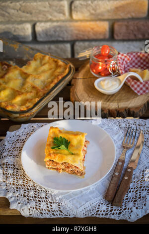 Klassische hommade Lasagne mit Bolognese Sauce auf Holztisch mit Spitze Tischdecke Stockfoto