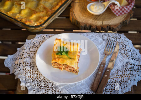 Klassische hommade Lasagne mit Bolognese Sauce auf Holztisch mit Spitze Tischdecke Stockfoto