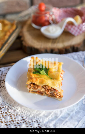 Klassische hommade Lasagne mit Bolognese Sauce auf Holztisch mit Spitze Tischdecke Stockfoto