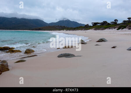 Strand am Wineglass Bay, Freycinet Nationalpark, Tasmanien mit Steinen in den Vordergrund und blaues Meer an einem bewölkten Tag Stockfoto