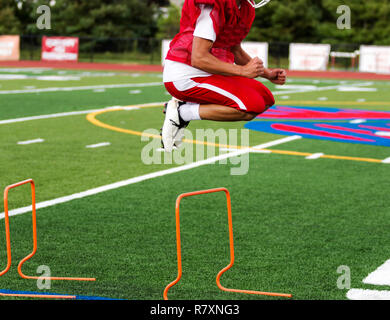 Ein High School Athlet springen über Hindernisse auf grünem Rasen Feld während der Saison Fußball-Praxis. Stockfoto