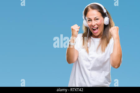 Mittleres Alter Hispanic Frau Musikhören mit Kopfhörern über isolierte Hintergrund sehr glücklich und aufgeregt, Sieger Geste mit erhobenen Armen, Stockfoto