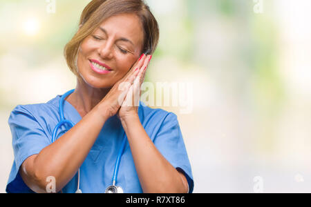 Mittleren Alters ältere Krankenschwester Arzt Frau über isolierte Hintergrund müde schlafen, träumen und mit den Händen posiert zusammen, während lächelnd mit geschlossenen Augen. Stockfoto