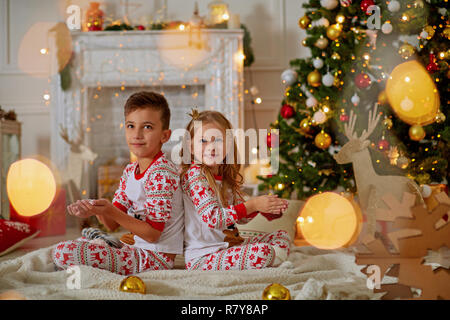 Kleine Kinder lachen in der Nähe des Weihnachtsbaums hinter dem grünen Türen und halten in ihren Händen nicht dämmernde Schnee Stockfoto