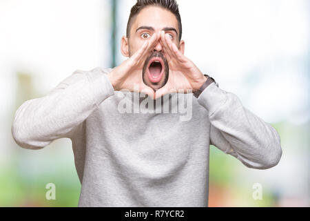 Jungen gutaussehenden Mann mit Sweatshirt über isolierte Hintergrund schrie wütend, laut mit den Händen über Mund Stockfoto