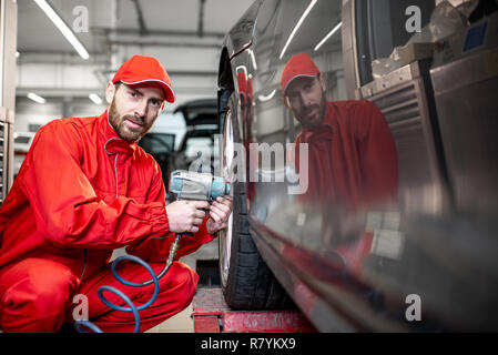 Auto service Arbeitnehmer in roter Uniform ändern Rad eines Sport Auto auf den Reifen Montage Service Stockfoto