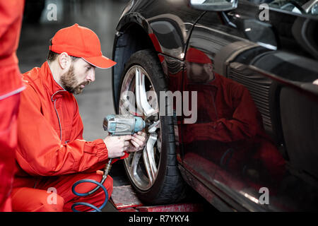Auto service Arbeitnehmer in roter Uniform ändern Rad eines Sport Auto auf den Reifen Montage Service Stockfoto