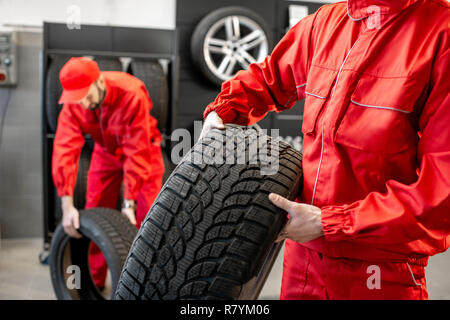 Arbeiter in Uniform tragen neue Reifen am Auto Service oder Store, Nahaufnahme Stockfoto