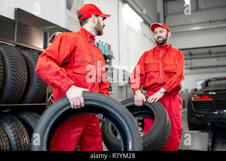 Auto service Arbeitnehmer in roter Uniform tragen neue Reifen auf den Reifen Montage Service oder Shop Stockfoto