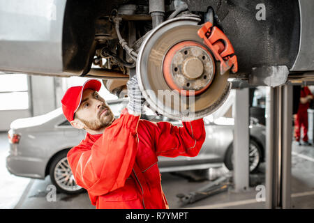 Automechaniker in Rot einheitliche Diagnose von Auto auf dem Hebezeug am Auto Service Stockfoto