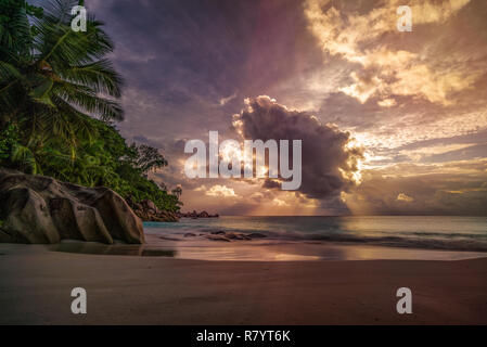 Sonnenstrahlen bei Sonnenuntergang hinter einer großen Wolke im Anse Georgette auf Praslin auf den Seychellen Stockfoto