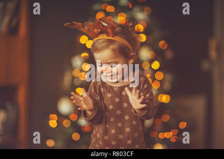 Baby für Kid's Christmas Party, süße kleine Baby in Rudolph Kostüm klatschen und genießen Matinee, mit Vergnügen, Urlaub in der Nähe von Weihnachten Baum Stockfoto