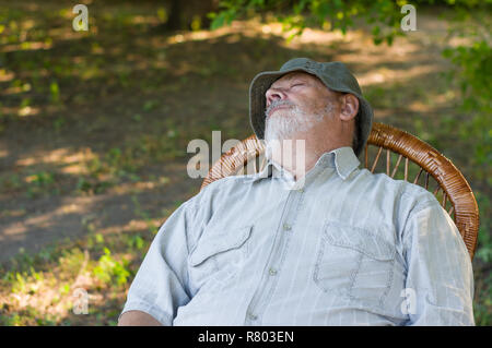 Outdoor Portrait der Kaukasischen älterer Mann schlafen in einem Korbstuhl im Sommer Park Stockfoto