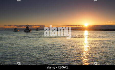 Sonnenuntergang spiegelt im Meer mit kleinen Fischerbooten in ruhigem Wasser verankert, Orford, Suffolk Stockfoto