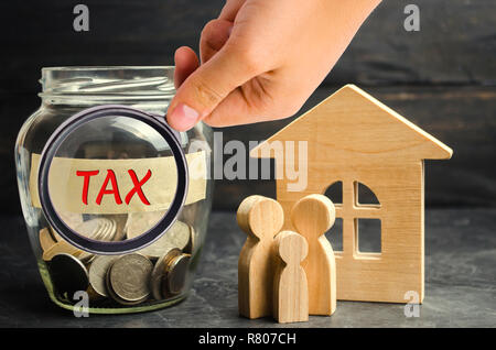 Glas Glas mit Münzen und die Inschrift "Steuer" und ein kleines Haus. Steuern auf Immobilien, Zahlung. Strafe, Verzug. Register der Steuerzahler für die Eigenschaft. Stockfoto