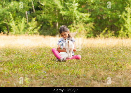 Mädchen mit weiße Katze sitzt auf Gras im Freien Stockfoto